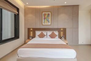 Une chambre moderne avec un grand lit, une tête de lit intégrant une œuvre d’art, des tables de chevet avec des lampes et une fenêtre équipée de stores.