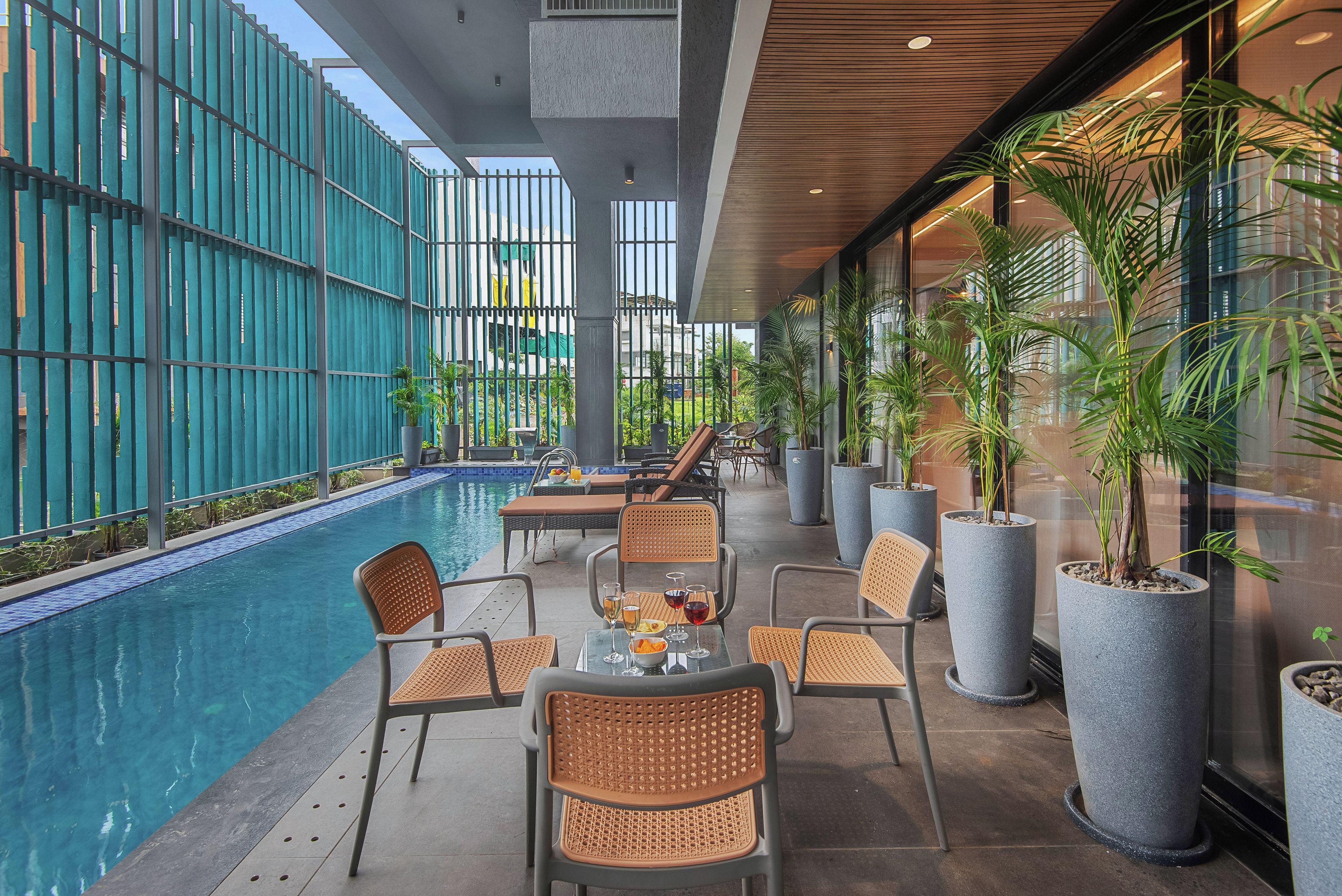 A poolside area with seating and a dining table, surrounded by potted plants and a view of the pool.