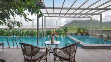 An outdoor pool area with two wicker chairs, a table with a vase of flowers, and a view of a mountainous landscape.