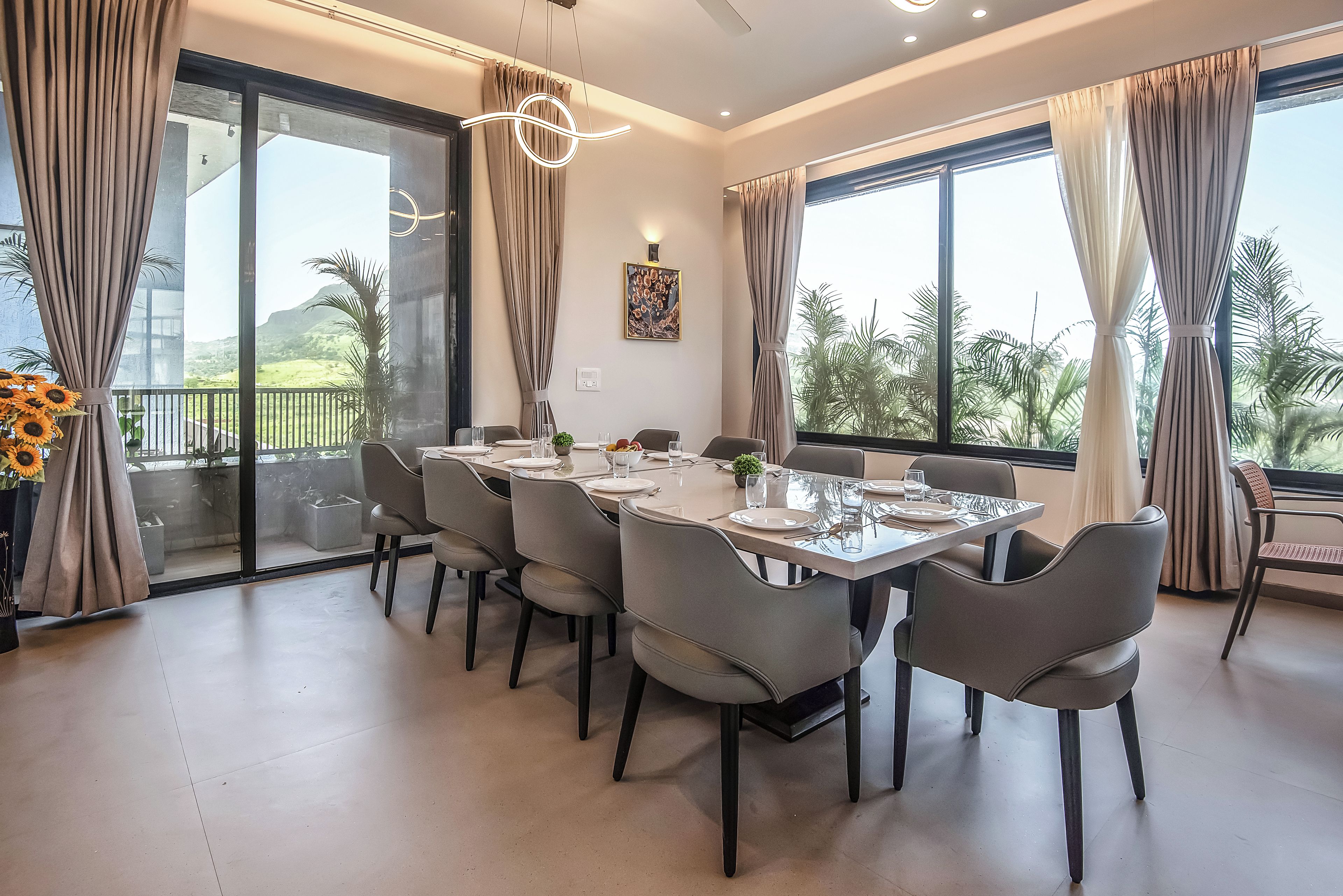 Un coin repas avec une grande table dressée pour six personnes, entourée de chaises, et offrant une vue sur la verdure à l’extérieur.