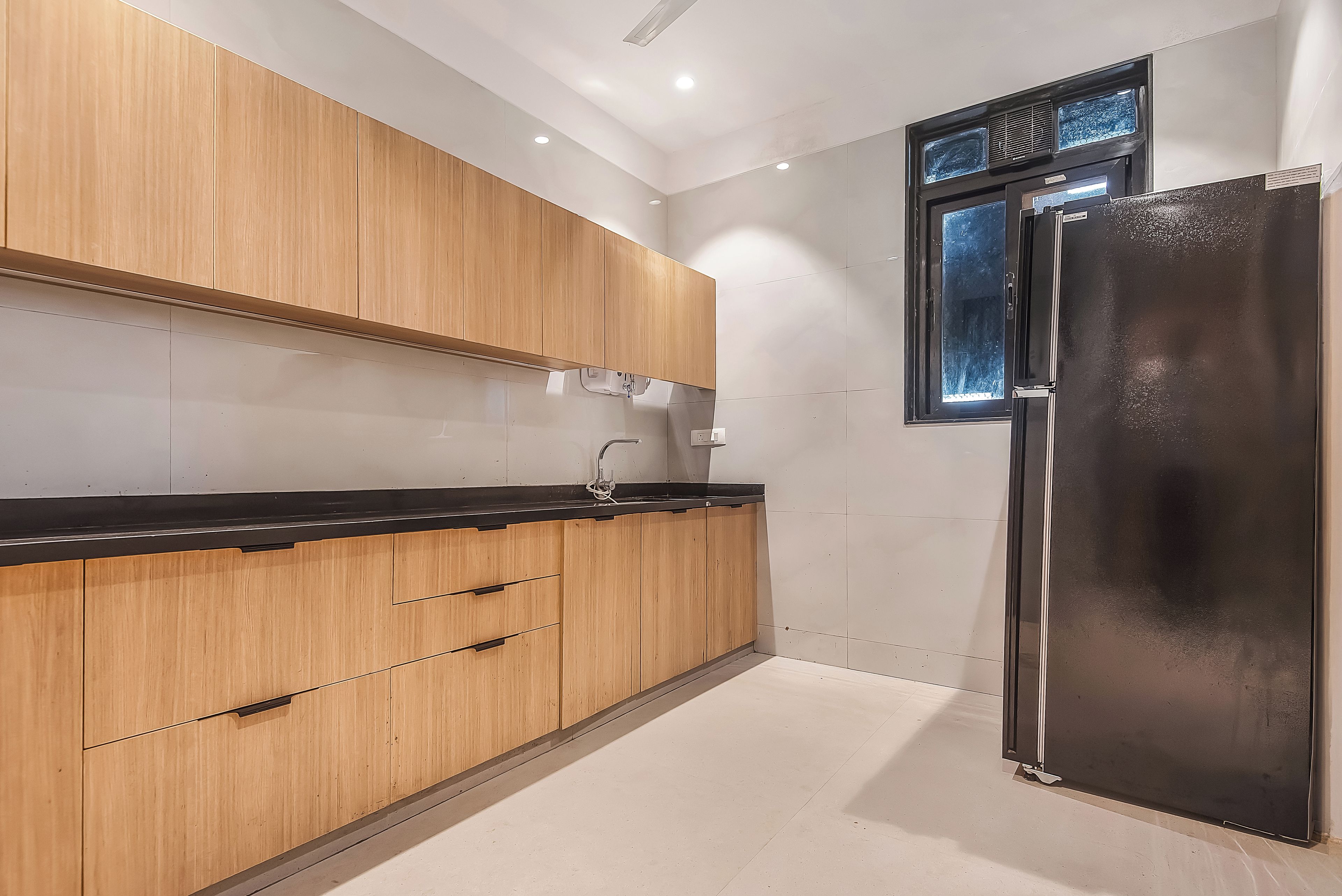 Cocina moderna con armarios de madera, encimera negra y refrigerador de acero inoxidable.
