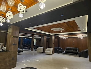 Una moderna área de recepción con mostrador, zona de estar con sofás y techo de madera con iluminación empotrada.