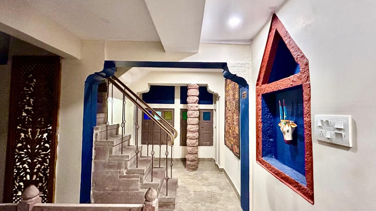 Una escalera con un muro azul decorativo, un pilar ornamental y un estante en la pared con un jarrón.