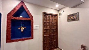 A hallway with a decorative wall-mounted shelf, a wooden door with intricate patterns, and a framed picture on the wall.