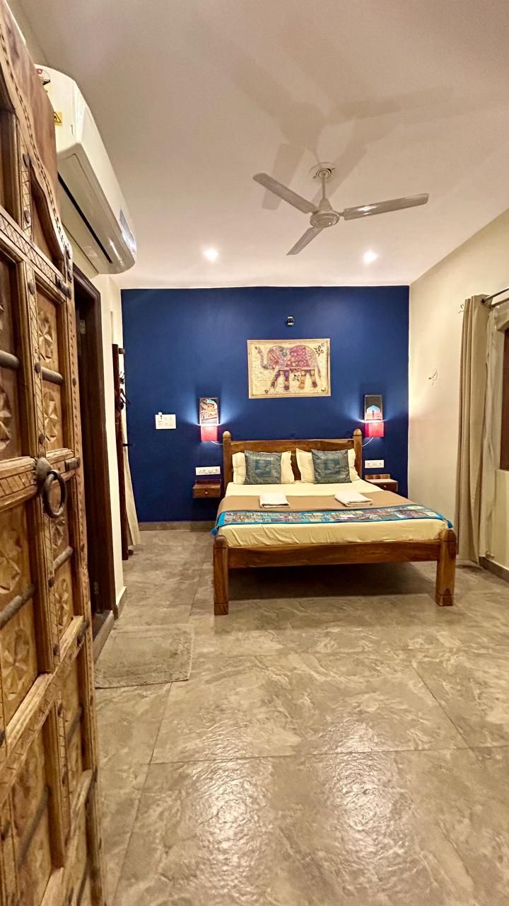 Quarto com cama, ventoinha no teto, ar condicionado fixado na parede e porta com detalhes elaborados.