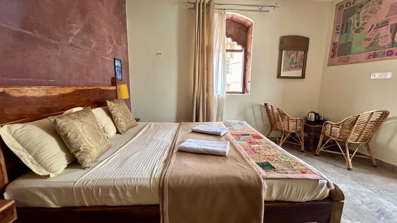 Una habitación con una cama, una ventana con cortinas, una silla y una pared con un cuadro enmarcado.