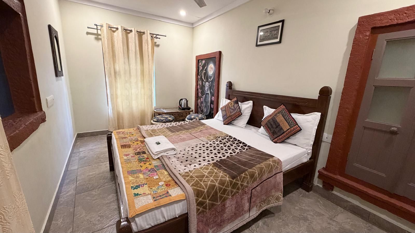 Un dormitorio con cama, mesita de noche, lámpara, ventana con cortinas y puerta.