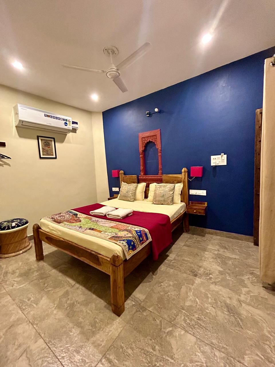 Un dormitorio con una cama, un ventilador de techo, un equipo de aire acondicionado, una mesita de noche y un espejo fijado a la pared.