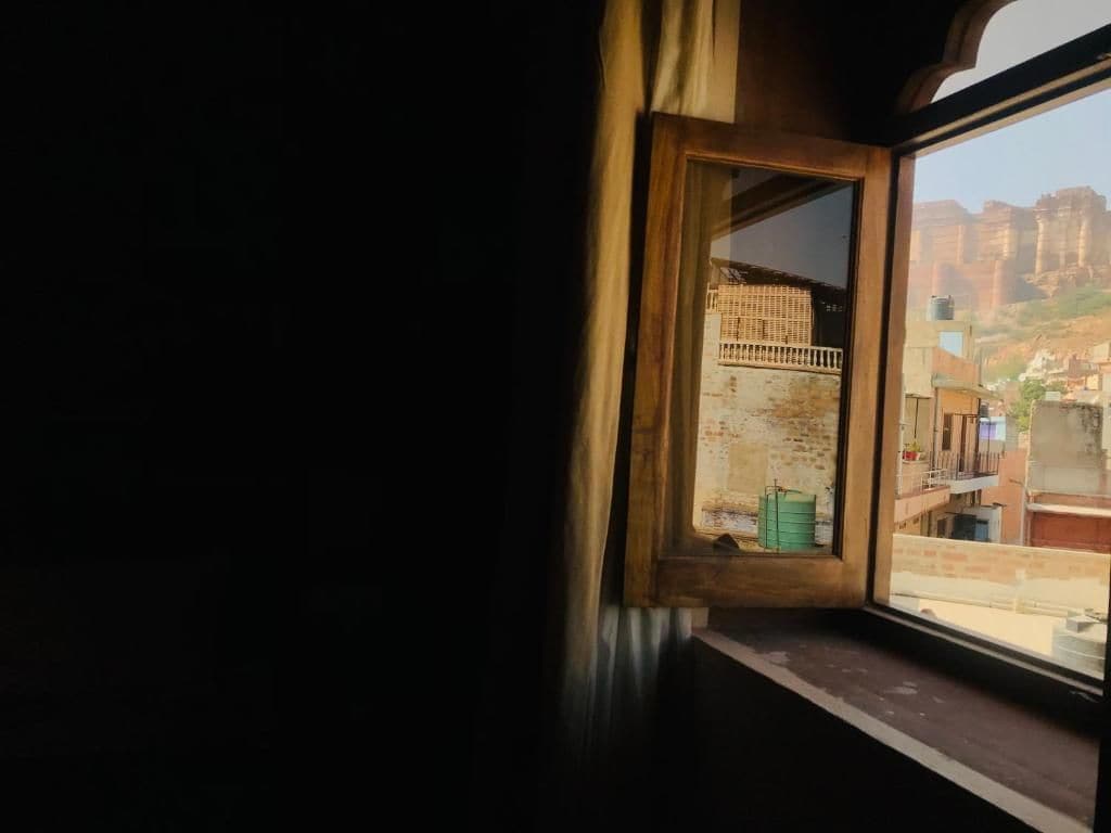 A window with a view of a building with a balcony and a green container on the windowsill.