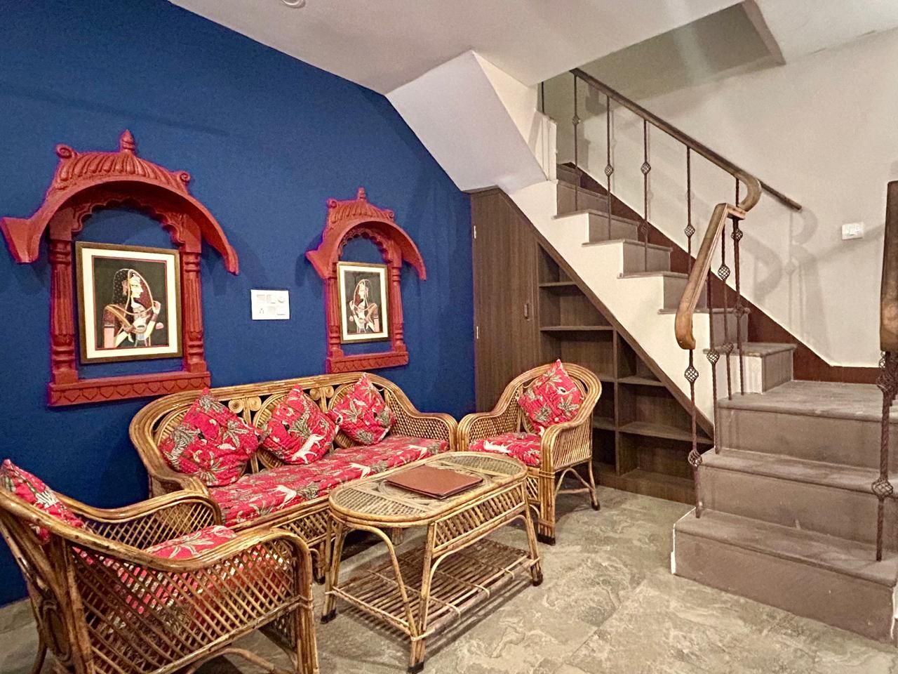 Ein Zimmer mit blauer Wand, zwei gerahmten Bildern, einer Rattan-Sofagarnitur, einem kleinen Tisch und einer Treppe.