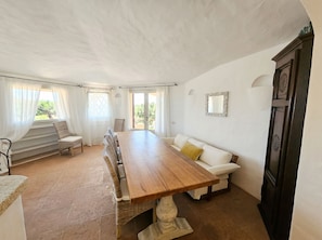 A dining area with a long wooden table, wicker chairs, a white sofa with a cushion, and a dark wooden cabinet. - Villa Marina – Front Marina Luxury Living in Porto Cervo (Porto Cervo)