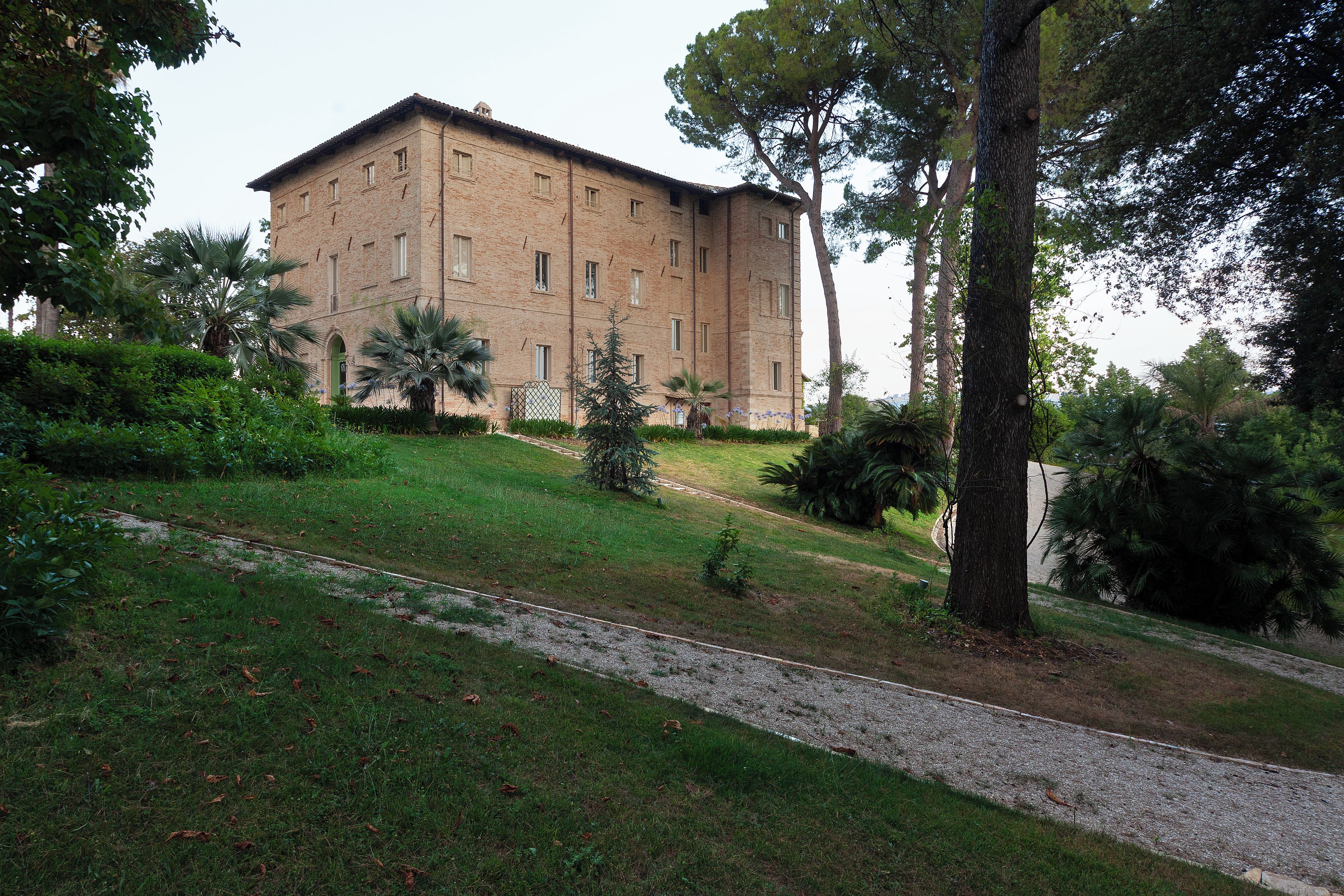 Un edifici de maó gran amb diverses finestres, envoltat d'un jardí ben cuidat i arbres.
