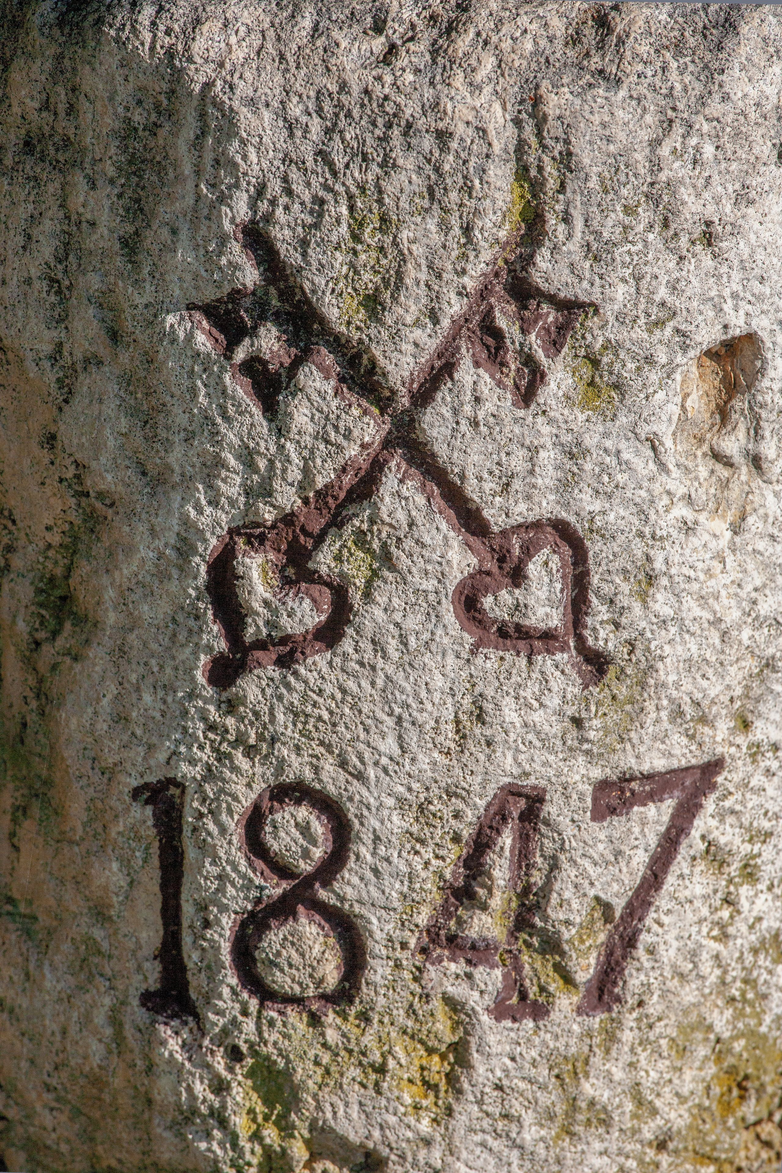 A close-up of a wall with a weathered inscription, including the numbers '1847' and a stylized 'X' symbol.