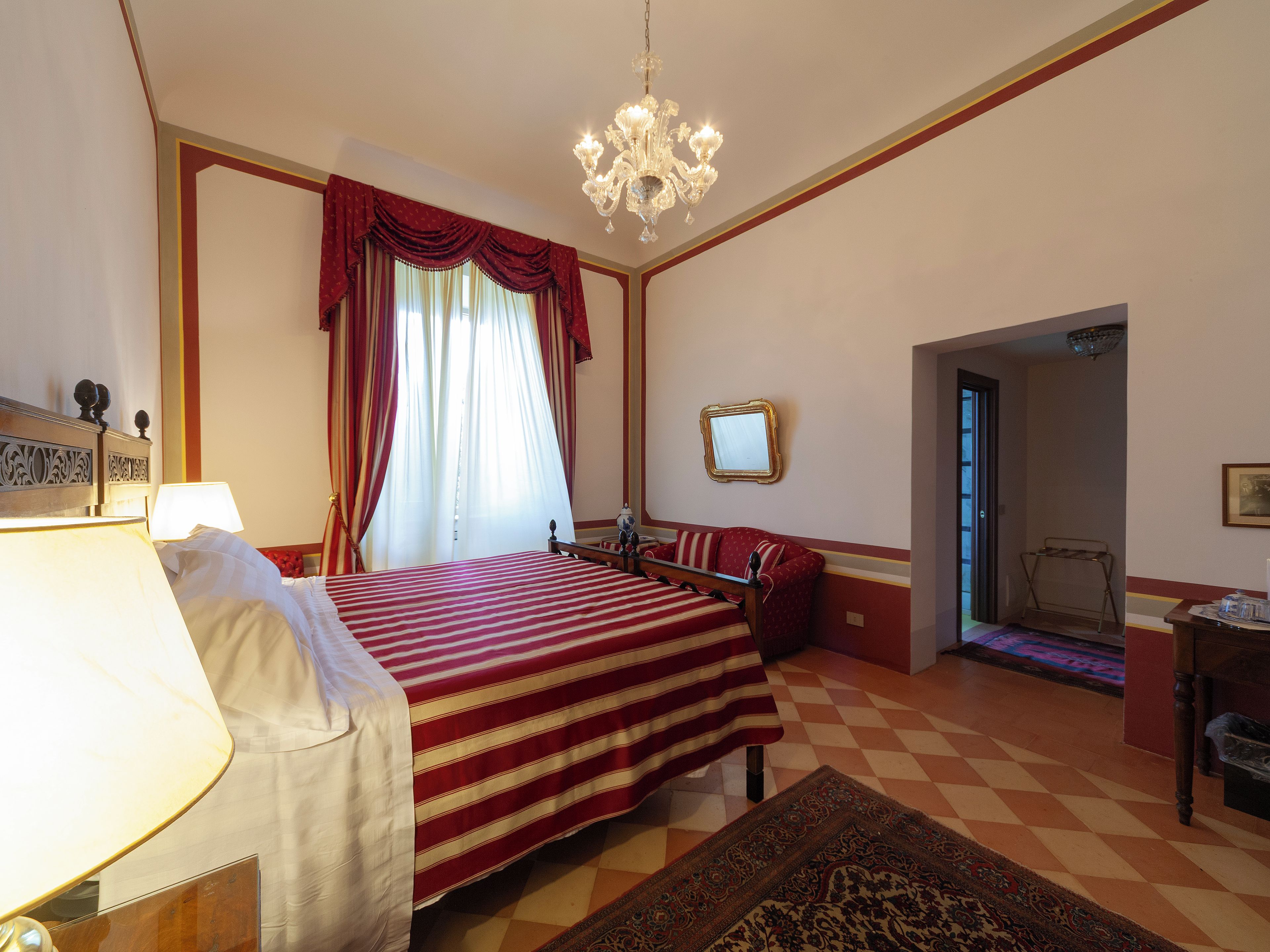 A hotel room with a bed, a chandelier, a mirror, and a checkered floor.