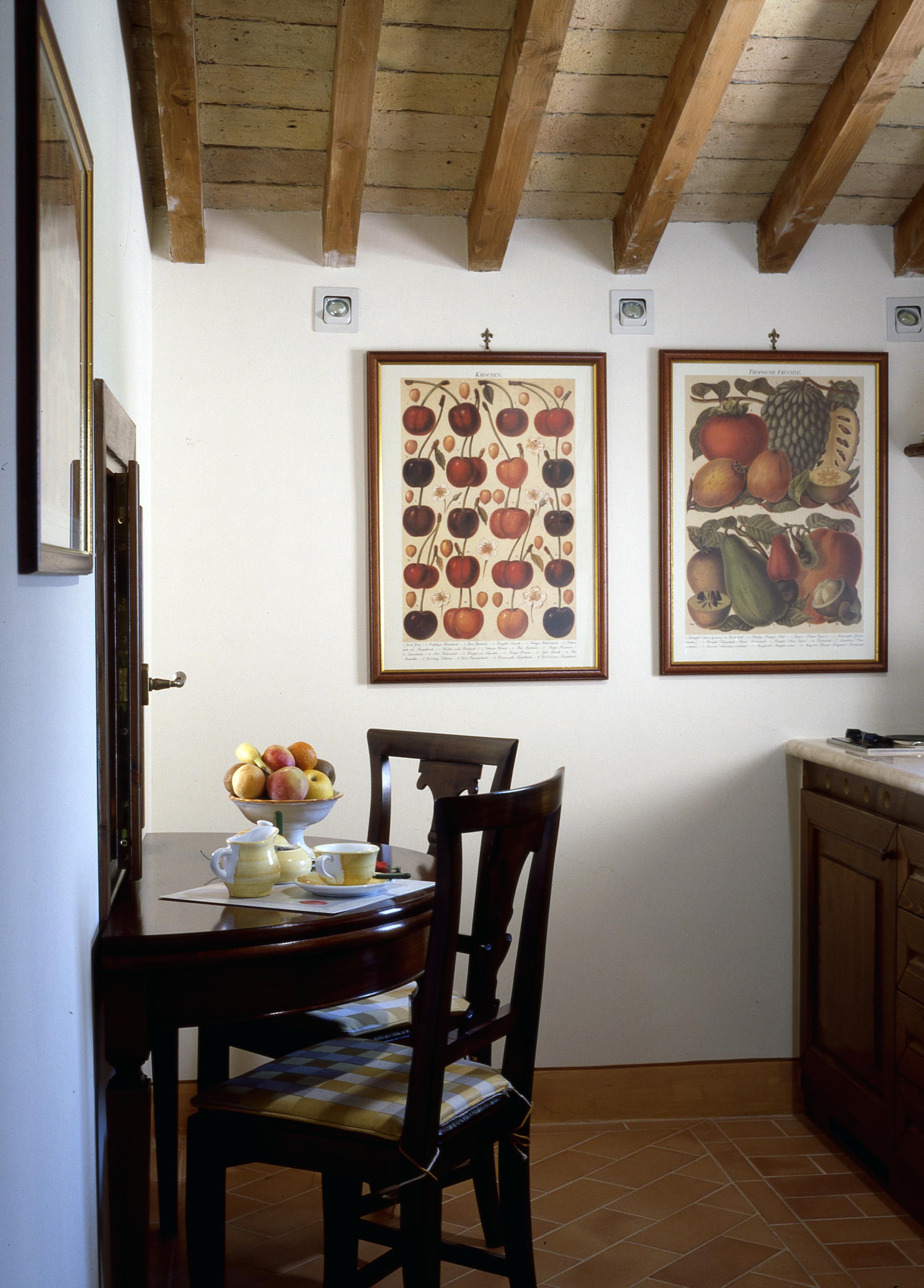 Un comedor con una mesa de madera, sillas y un cuenco de fruta. En la pared, dos láminas enmarcadas con motivos botánicos.