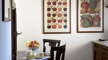 Un comedor con una mesa de madera, sillas y un cuenco de fruta. En la pared, dos láminas enmarcadas con motivos botánicos.