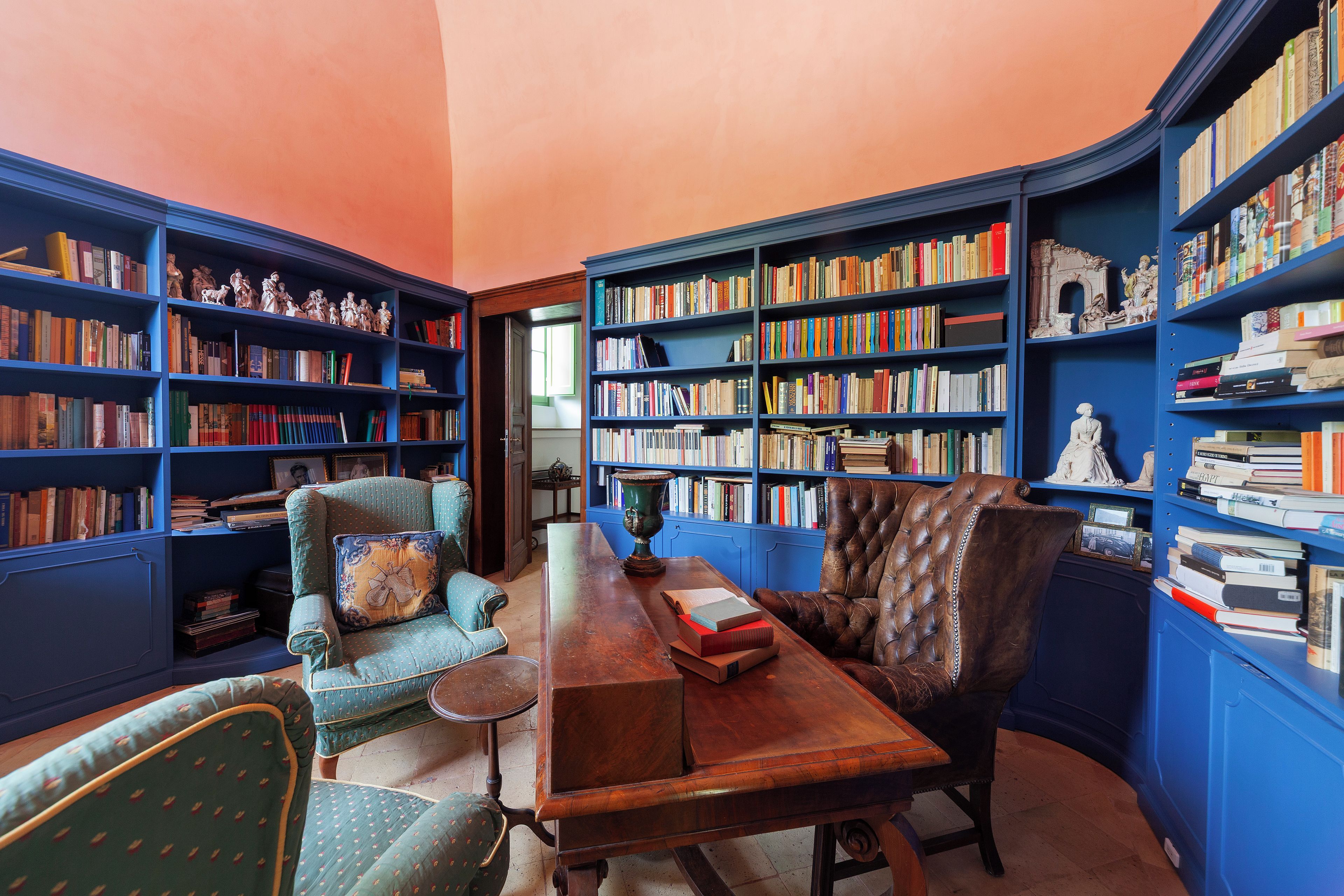 Eine Bibliothek mit Bücherregalen, einem Holztisch, zwei Stühlen und einer Zierdevas.
