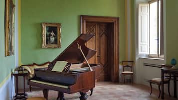 Um quarto com um piano de cauda, uma porta de madeira, um quadro emoldurado e uma janela.