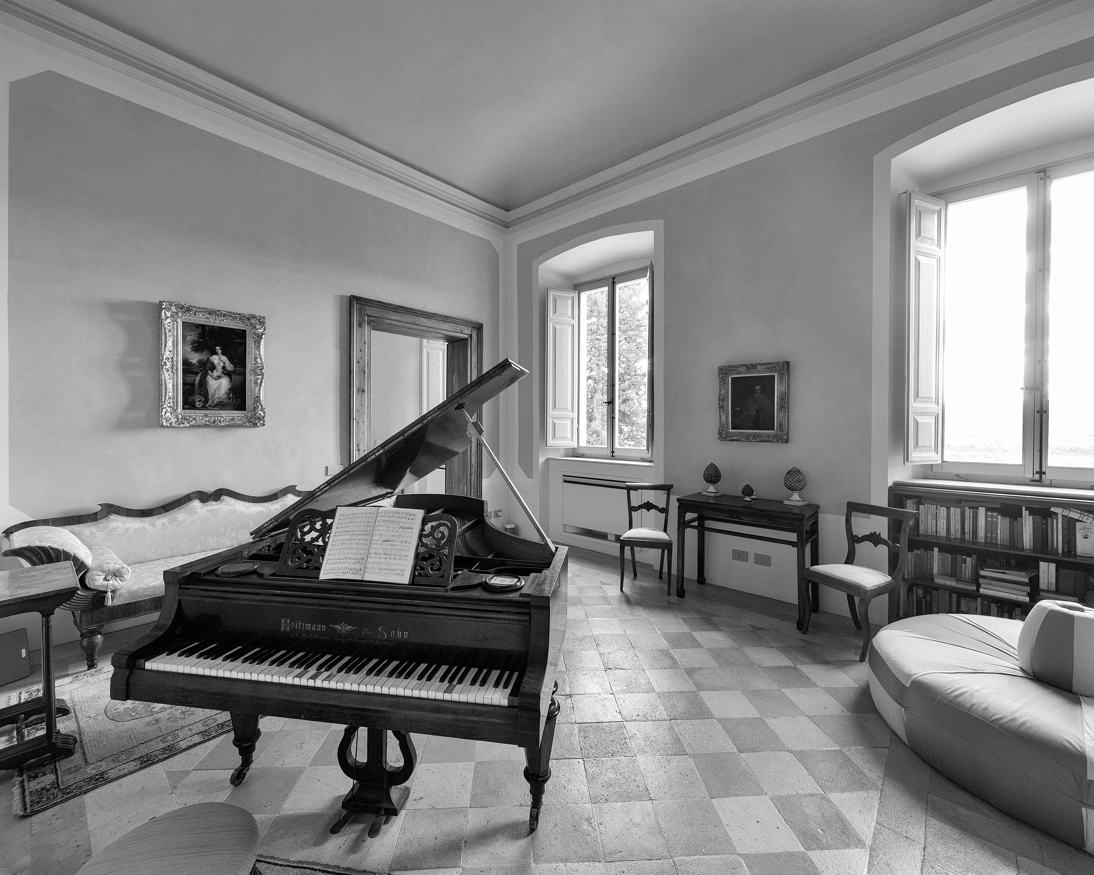 Un pianoforte a coda in un'ampia stanza con pavimento a scacchi, un divano e una libreria.