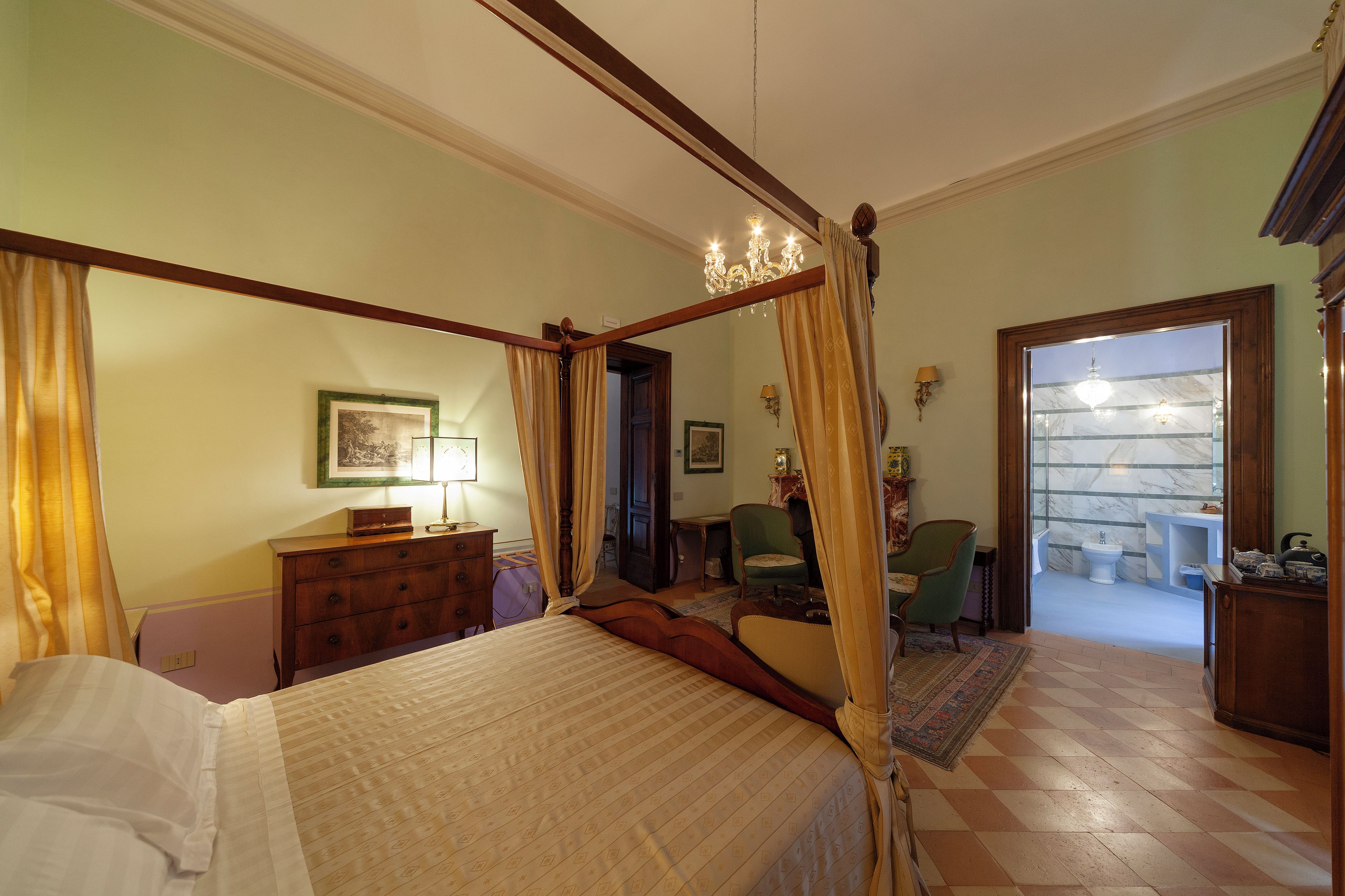 A bedroom with a four-poster bed, a chandelier, and a view of a bathroom through an open door.