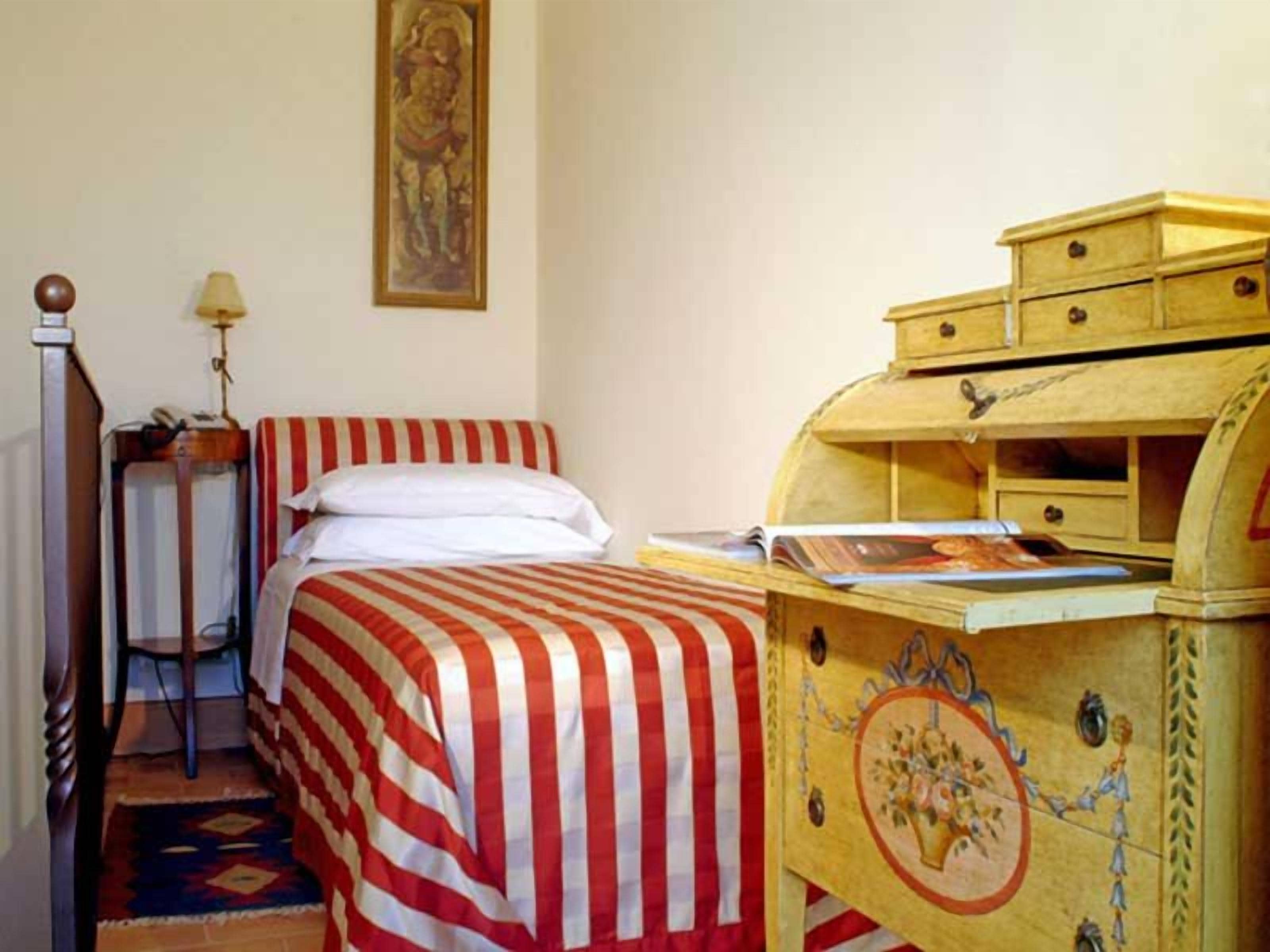 Una habitación con una cama, un aparador de madera, una lámpara y un cuadro en la pared.