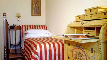 A room with a bed, a wooden chest of drawers, a lamp, and a framed picture on the wall.