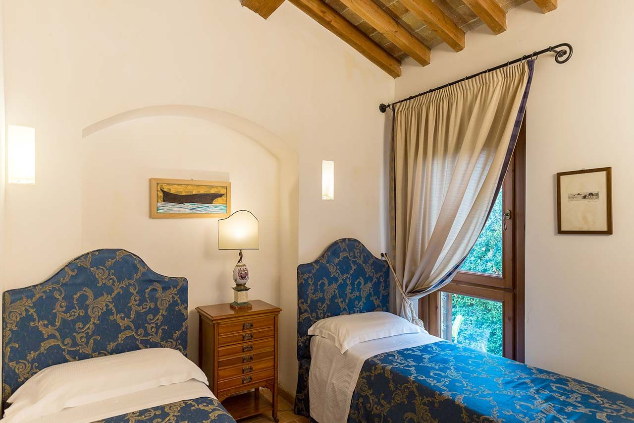 A bedroom with two beds, a nightstand, a lamp, a painting, and a window with curtains.