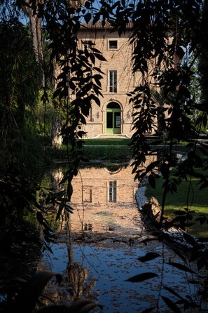 Un edificio histórico con una puerta verde, rodeado de árboles y un cuerpo de agua.