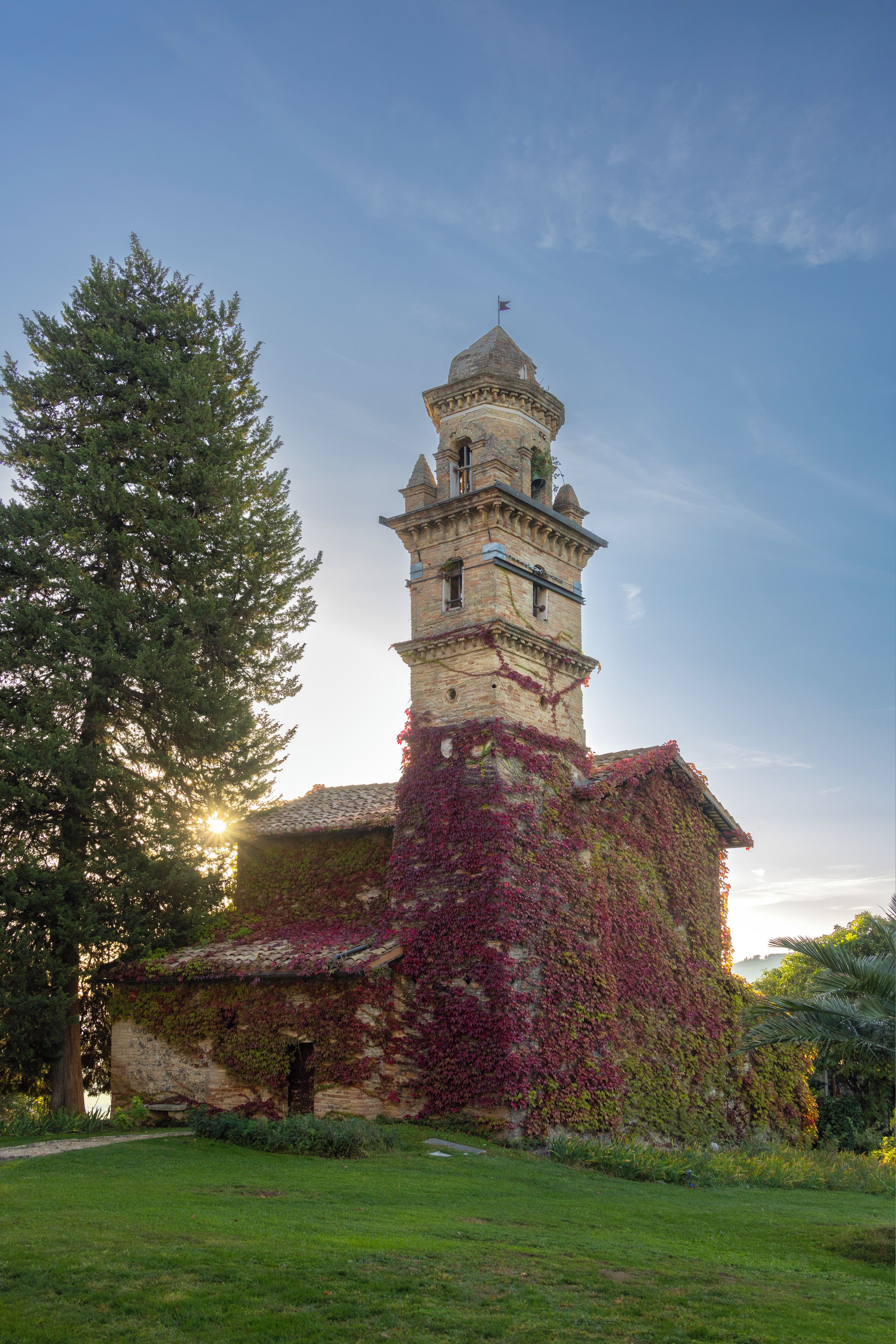 A historic tower with a clock, surrounded by greenery and a clear sky.