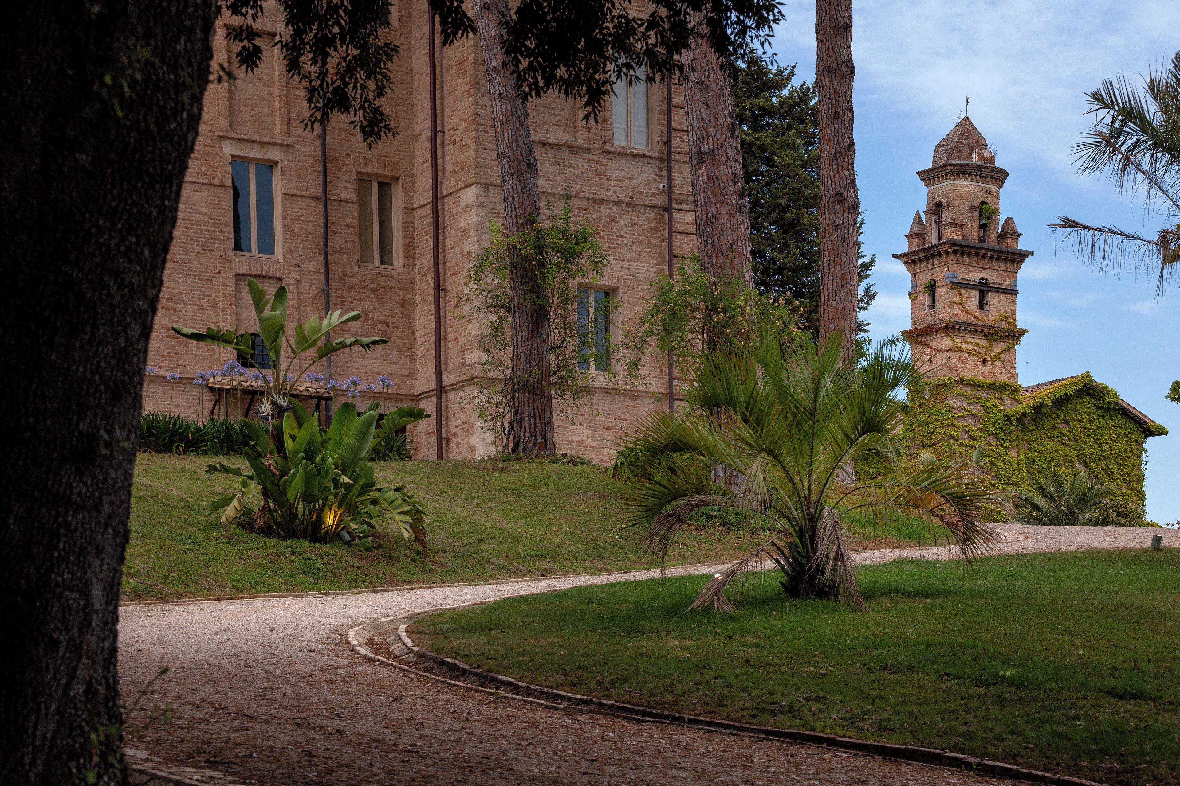 A historic building with a tower, surrounded by a well-maintained garden with various plants and a gravel pathway.