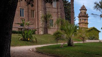 A historic building with a tower, surrounded by a well-maintained garden with various plants and a gravel pathway.