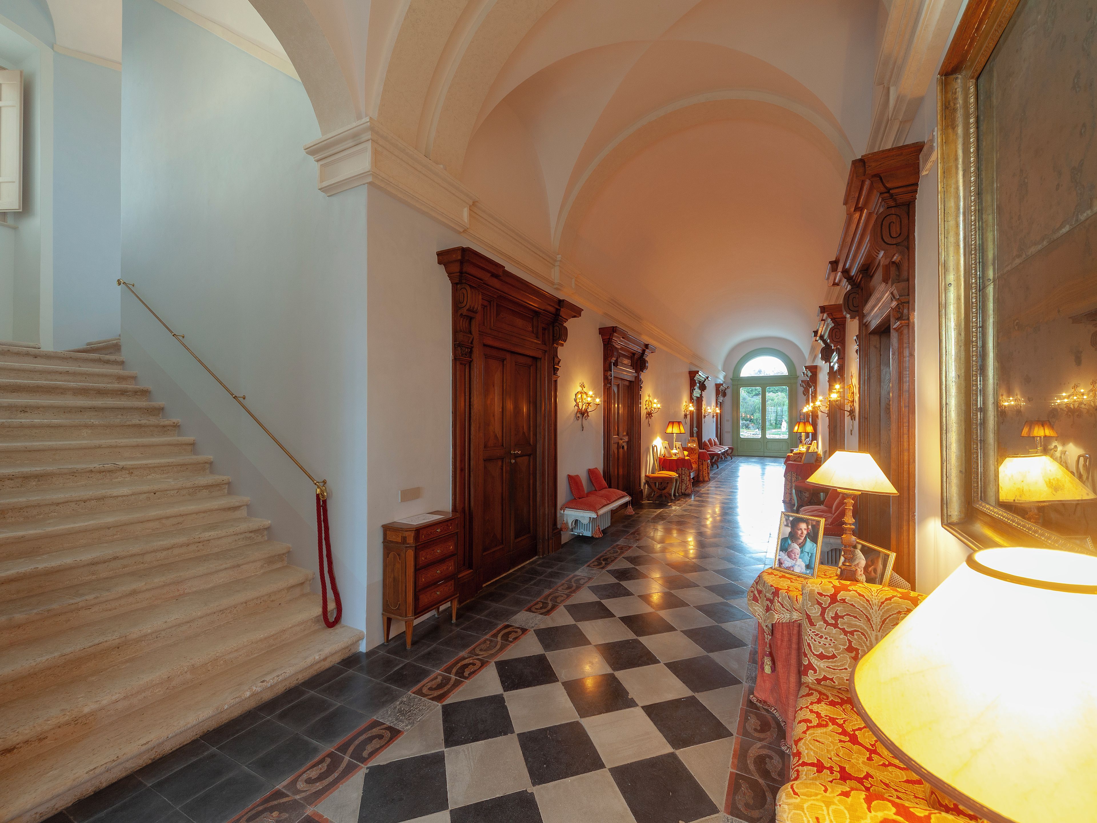 A grand hallway with a checkered floor, a staircase on the left, and a large mirror on the right.