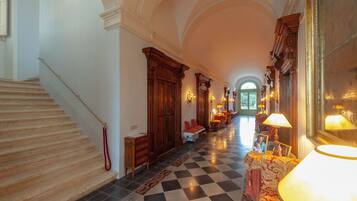 A grand hallway with a checkered floor, a staircase on the left, and a large mirror on the right.