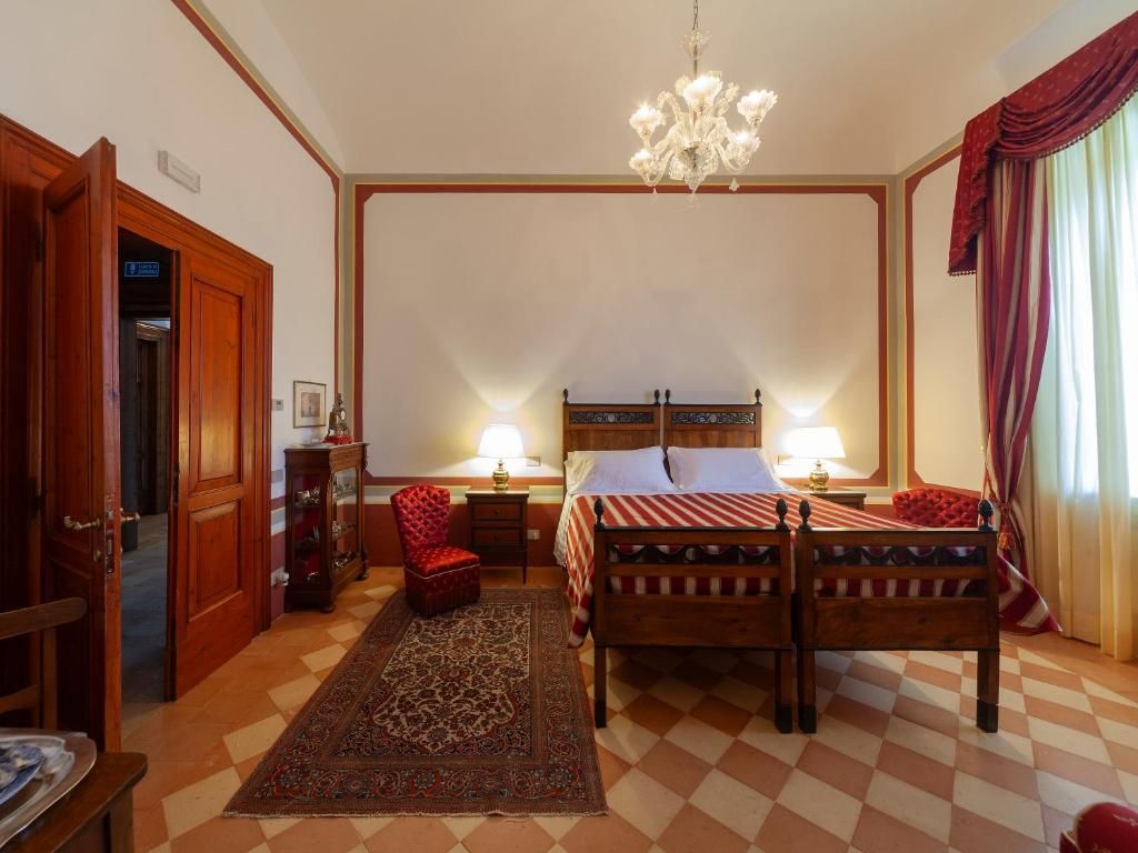 A bedroom with a checkered floor, a wooden bed with a striped bedspread, a chandelier, and a red curtain.