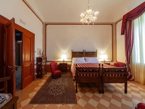 A bedroom with a checkered floor, a wooden bed with a striped bedspread, a chandelier, and a red curtain.
