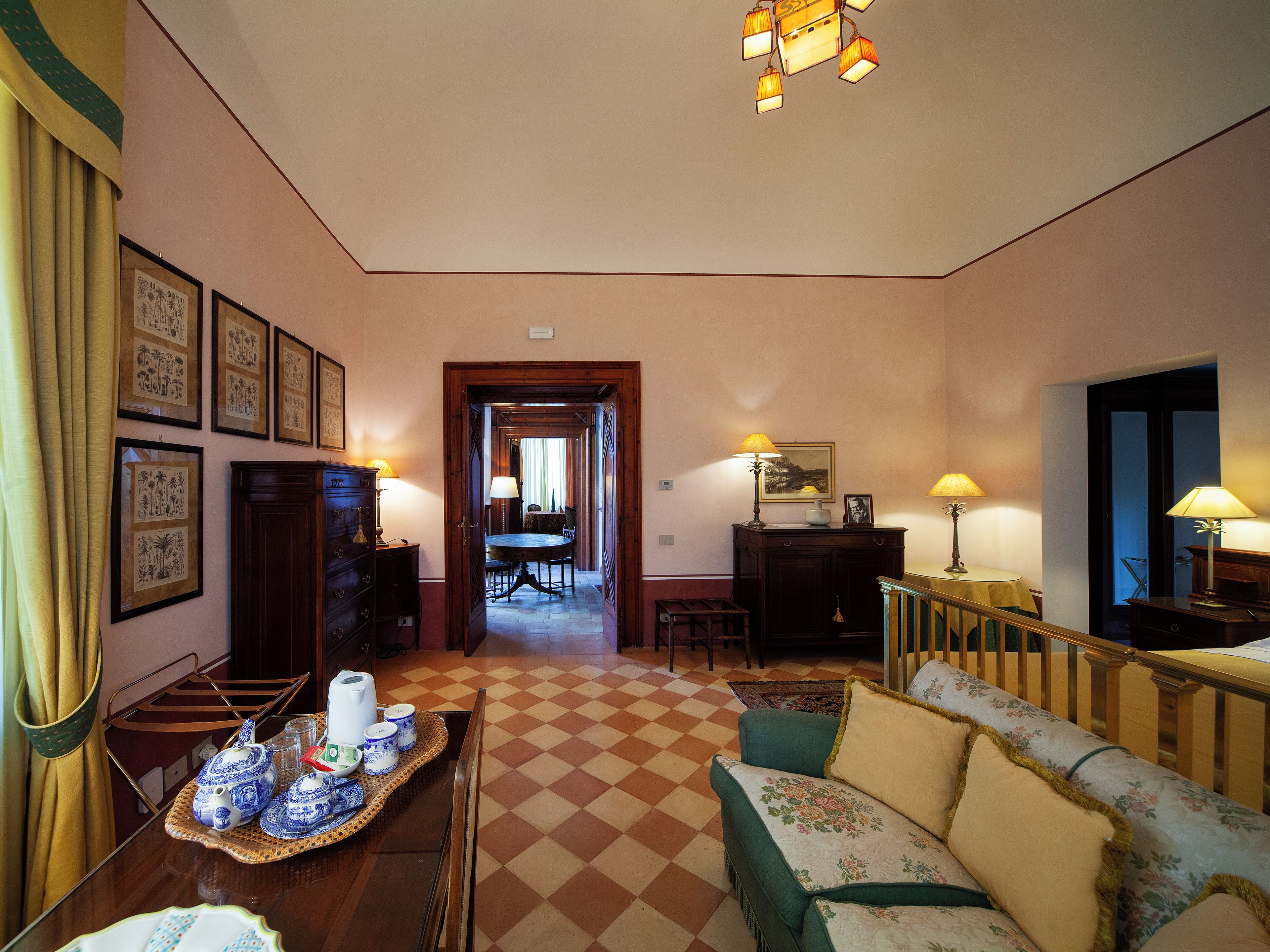 A room with a checkered floor, a sofa, a dining table with a tray of teapots, and framed pictures on the wall.
