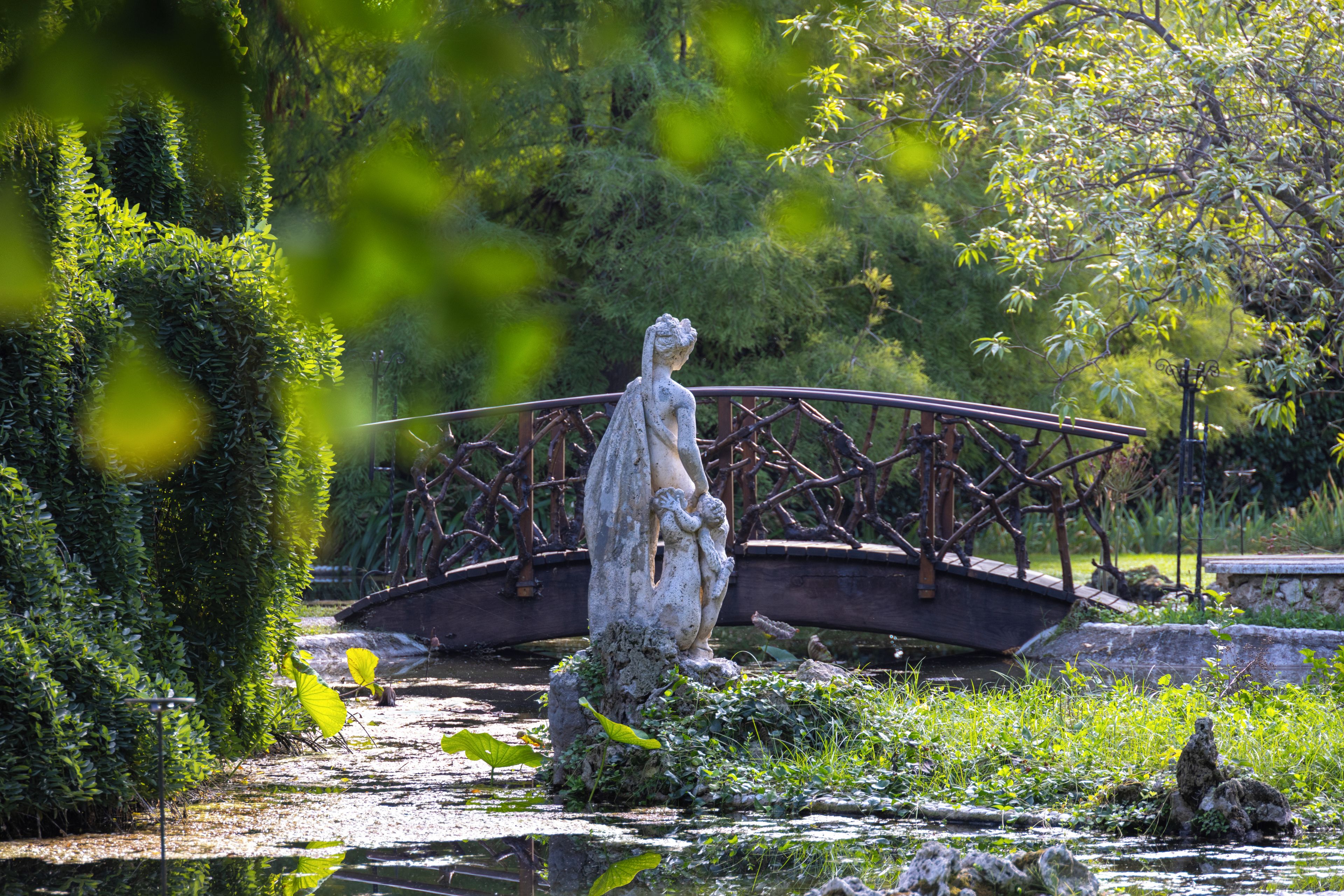 A garden with a statue, a bridge, and a pond.