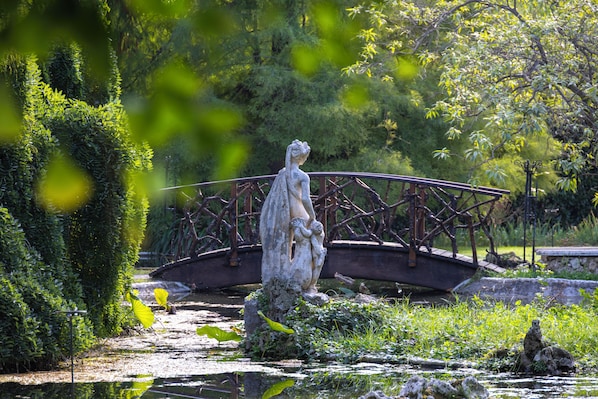 A garden with a statue, a bridge, and a pond.