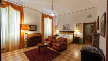 A hotel room with a bed, two armchairs, a small table, a lamp, a rug, and a fireplace.