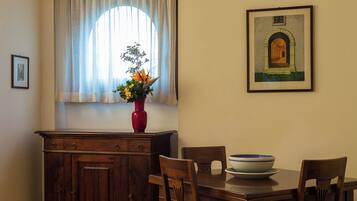 Un comedor con una mesa de madera, sillas, un florero con flores, una ventana con cortinas y un cuadro en la pared.