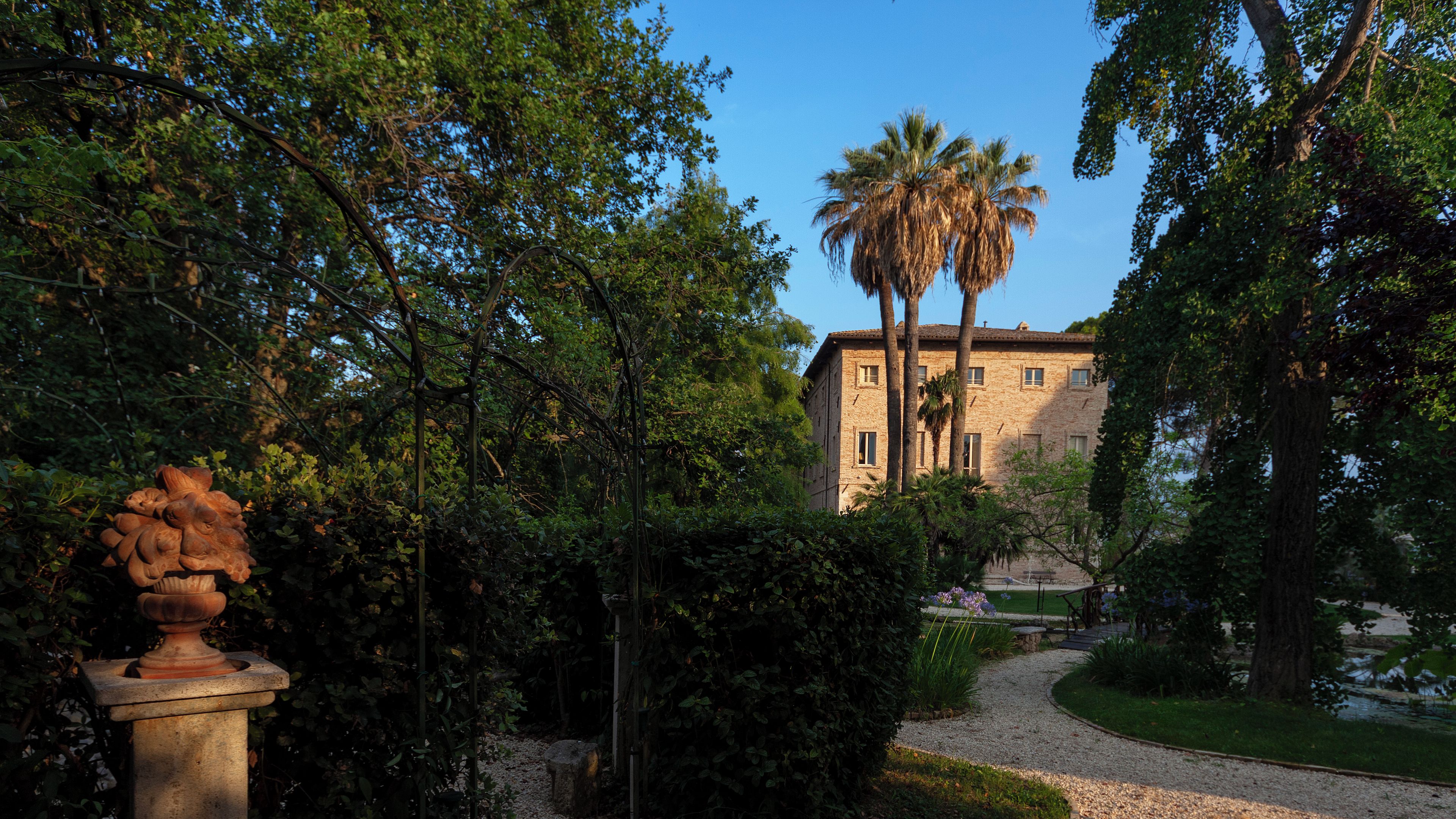 A building with a stone facade, surrounded by lush greenery and a gravel pathway.