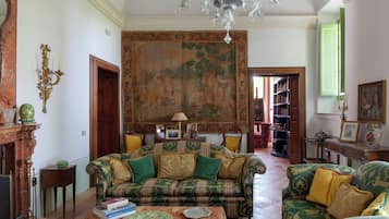 Ein traditionell eingerichtetes Wohnzimmer mit einem großen Wandteppich, einer Kristallleuchter und klassischen Möbeln.