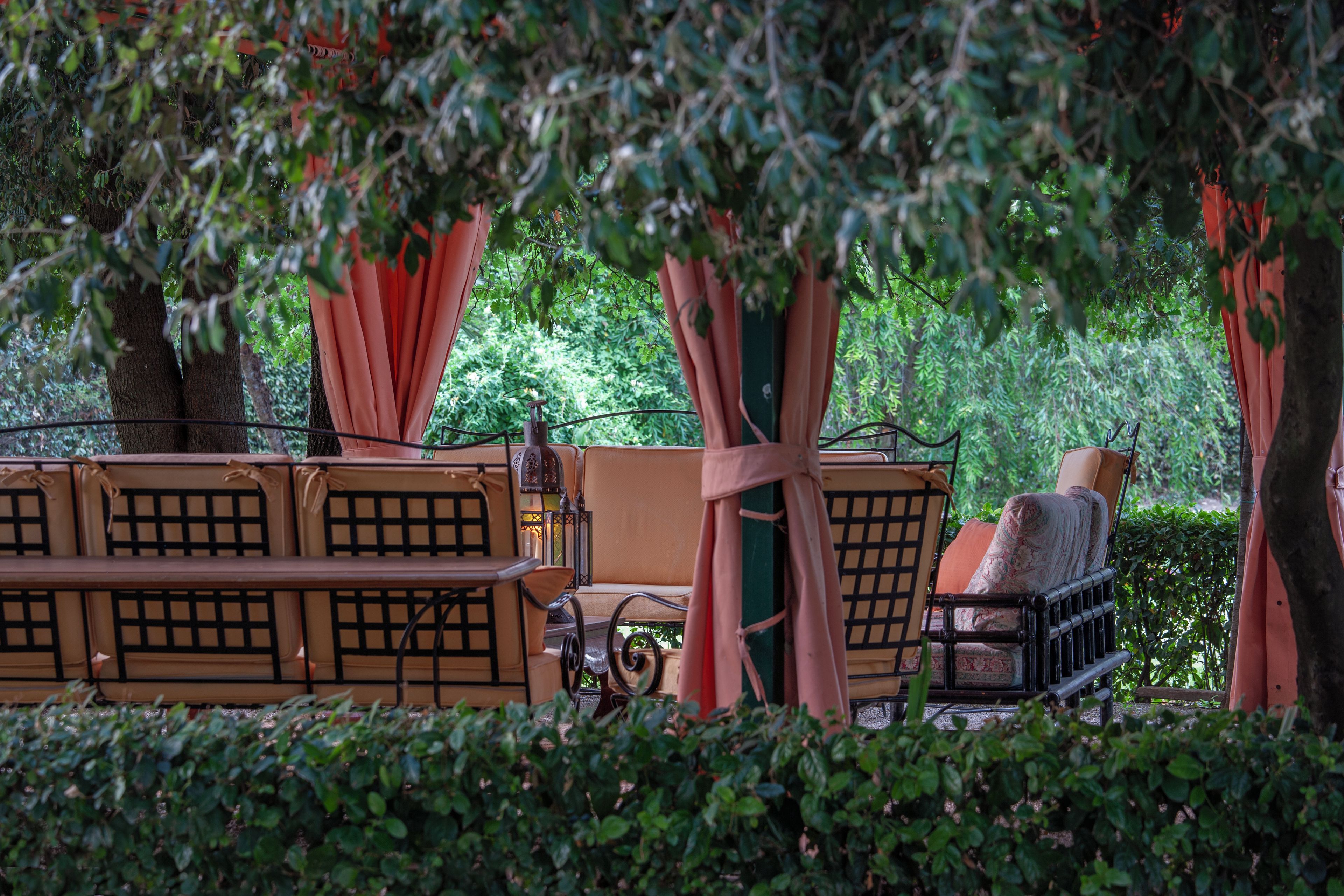 A seating area with cushioned benches and chairs, surrounded by trees and greenery.