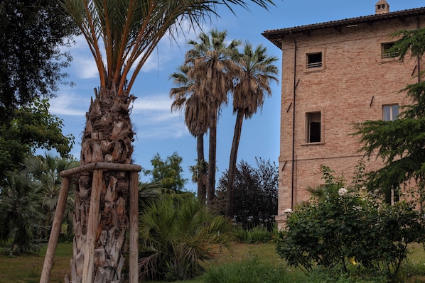 A rustic brick building with a garden, palm trees, and a wooden structure.