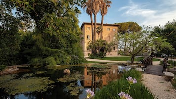 Ein friedlicher Garten mit Teich, einer Holzbrücke und einem Gebäude mit Stein-Fassade.