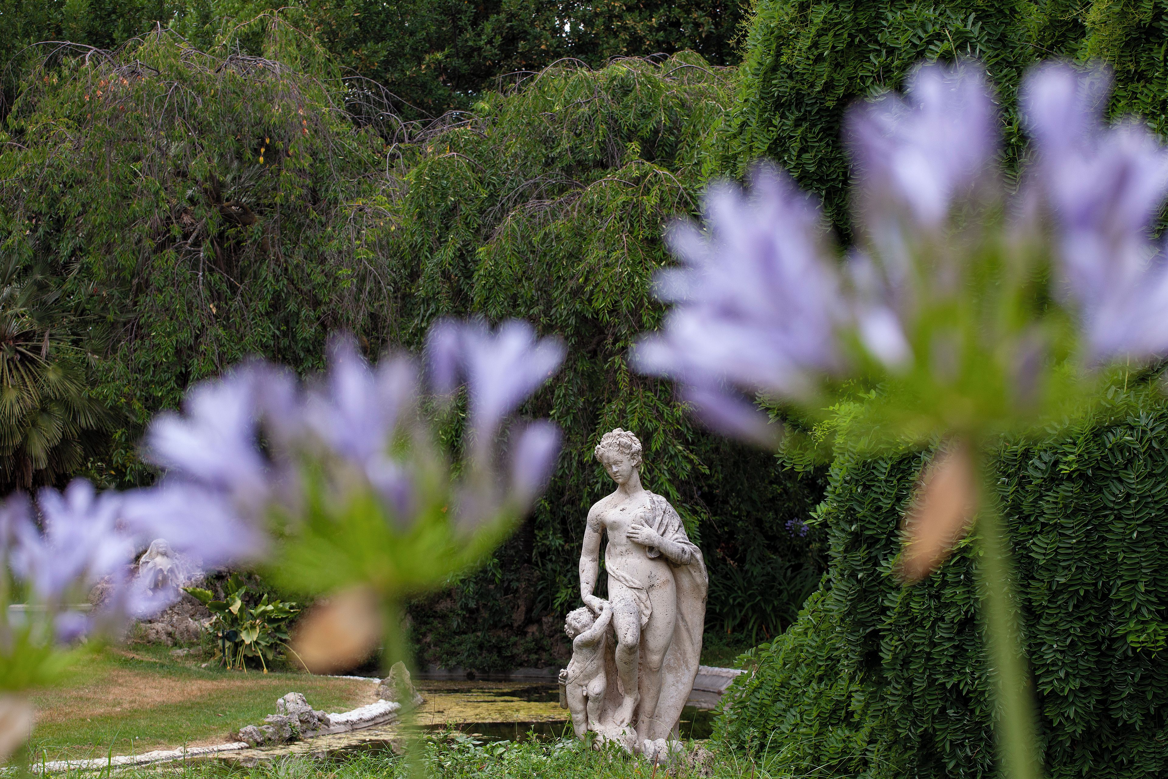 Uma estátua em um jardim com vegetação densa ao fundo.