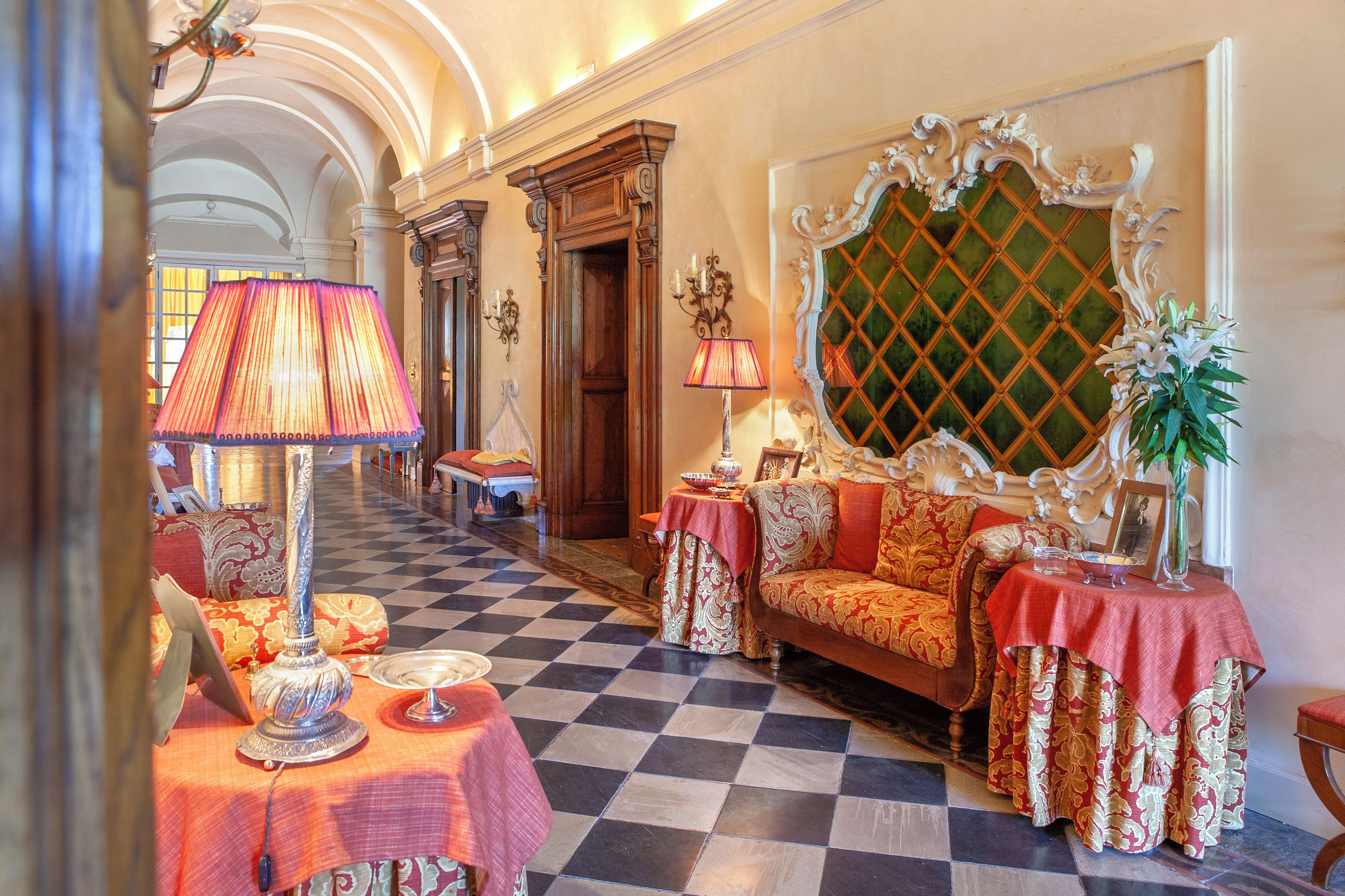 A hotel lobby with a checkered floor, ornate sofas, a grand mirror, and a chandelier.