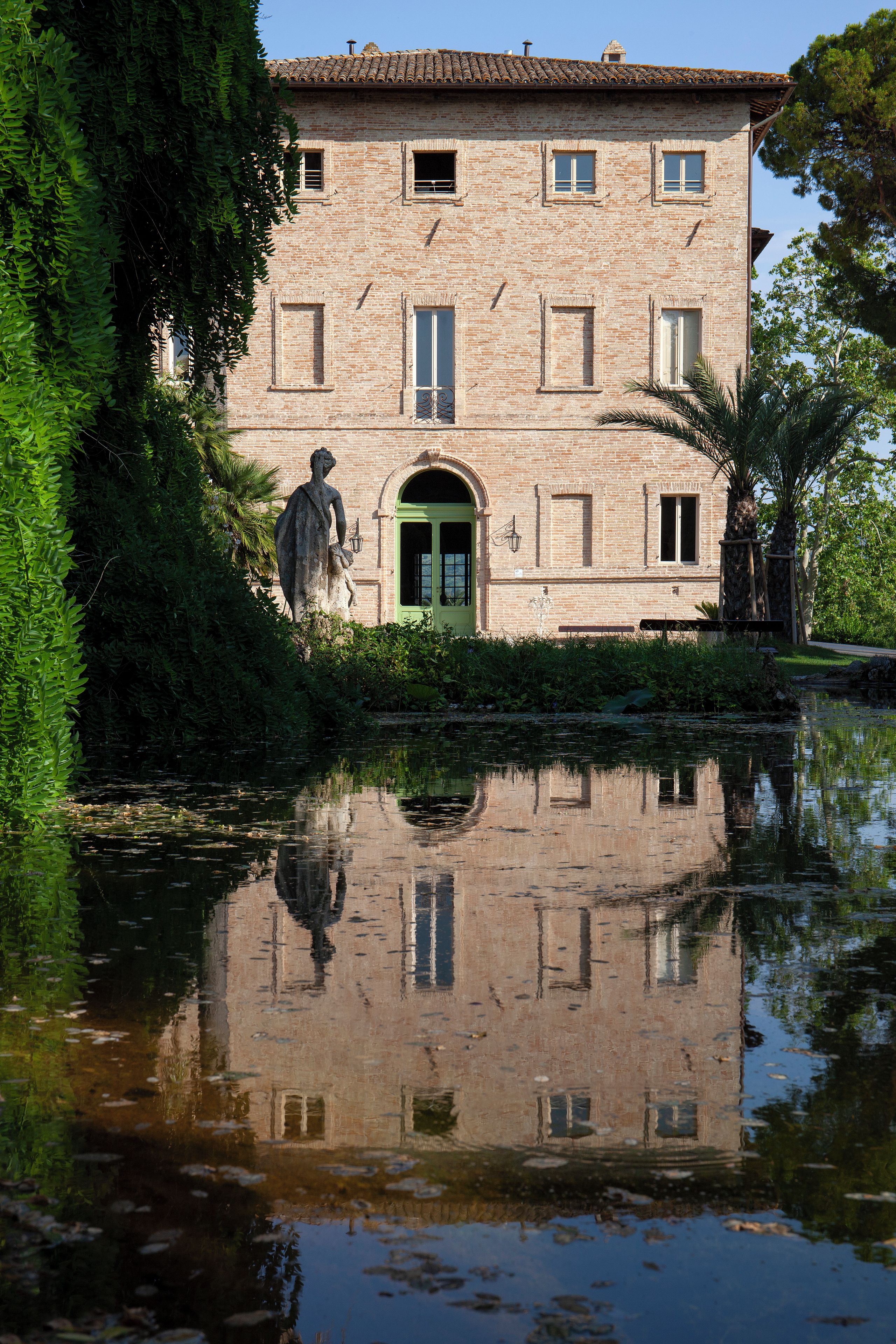 A historic building with a green door, a statue in front, and a reflection in the water.