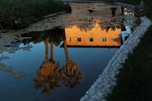 A building with a brick facade and multiple windows, reflected in a calm body of water.