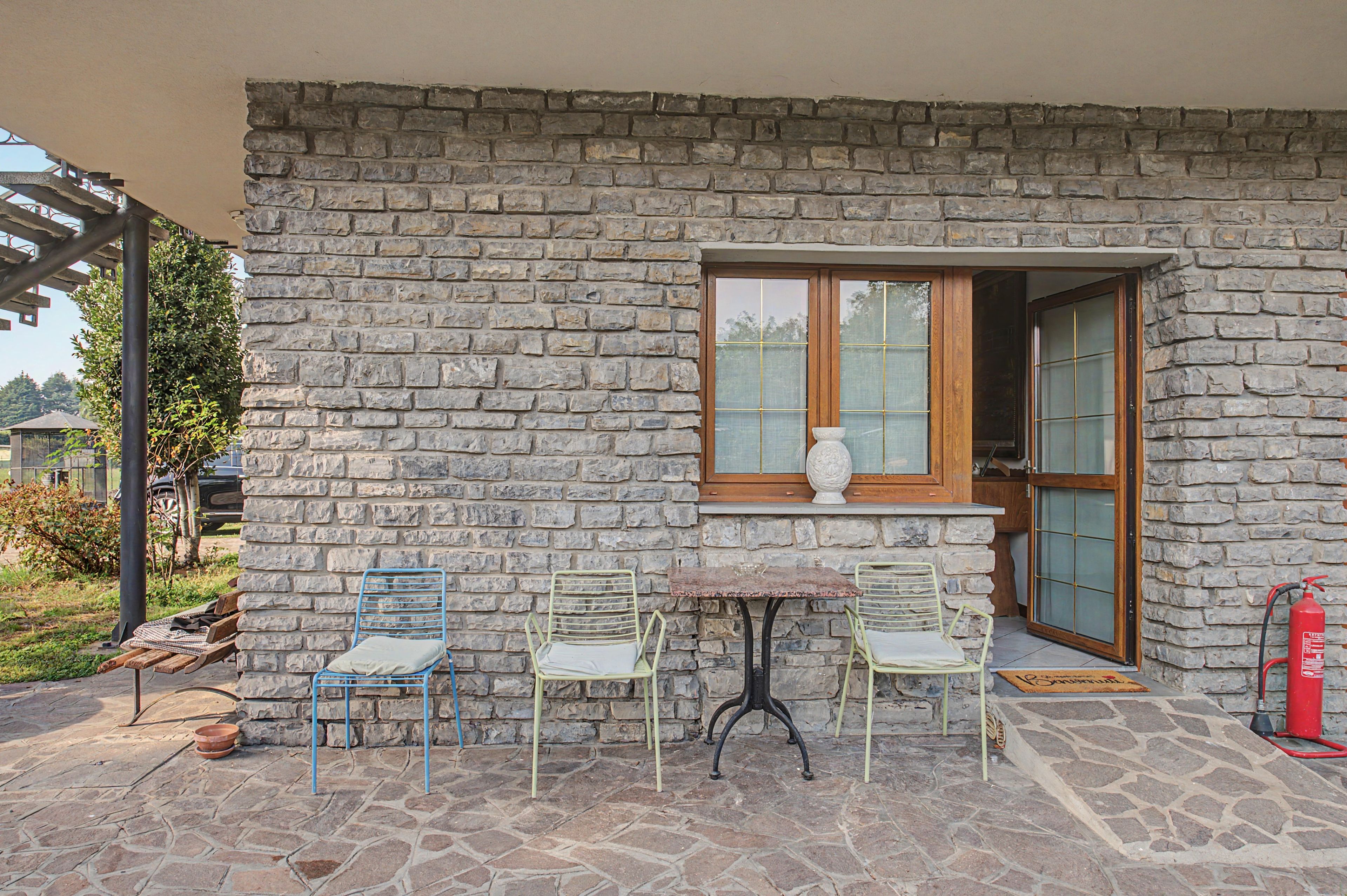 Un edificio de piedra con una ventana, dos sillas, una mesa y un extintor.
